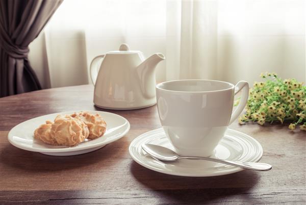 یک فنجان چای با قوری و کلوچه در بشقاب روی میز سبک سبک جذاب