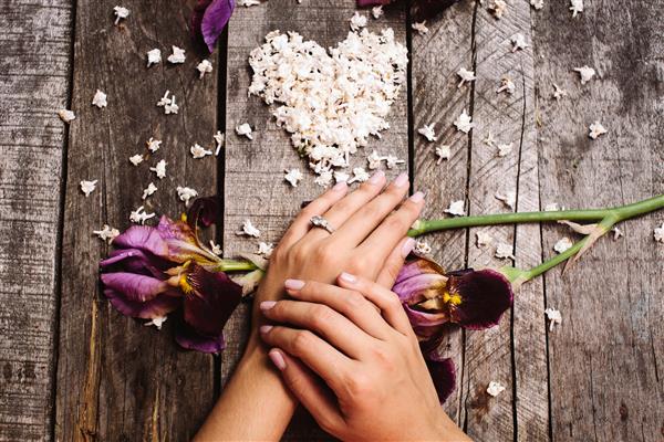 انگشتر عروسی پیشنهادی از نزدیک با شکل قلب گل های یاس بنفش و زنبق بنفشه در نمای بالایی میز چوبی