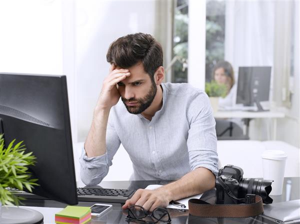 پرتره از تاجر جوان نگران و نشسته جلوی کامپیوتر در دفتر