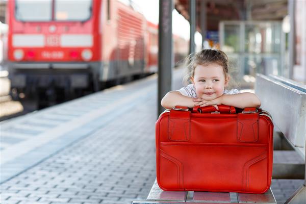 دختر کوچک ناز با چمدان قرمز بزرگ در ایستگاه راه آهن سفر