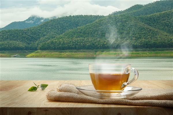 لیوان چای با گل میناکاری روی میز چوبی و زمینه باتلاق
