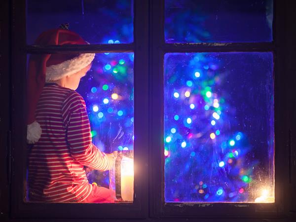 پسر ناز روی سپر پنجره نشسته شب ها با تلفن همراه بازی می کند وقت کریسمس منتظر بابانوئل است فیلتر آبی اعمال می شود