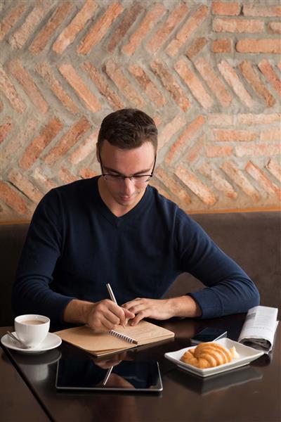 یک تاجر خندان در حالی که در کافه قهوه صبحانه می نوشید در دفتر یادداشت یادداشت وکتور می کند