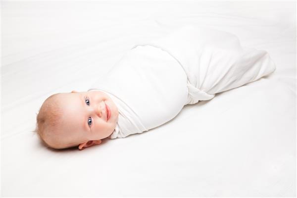 کودک در پتو سفید که روی تخت خوابیده بود قنداق شد