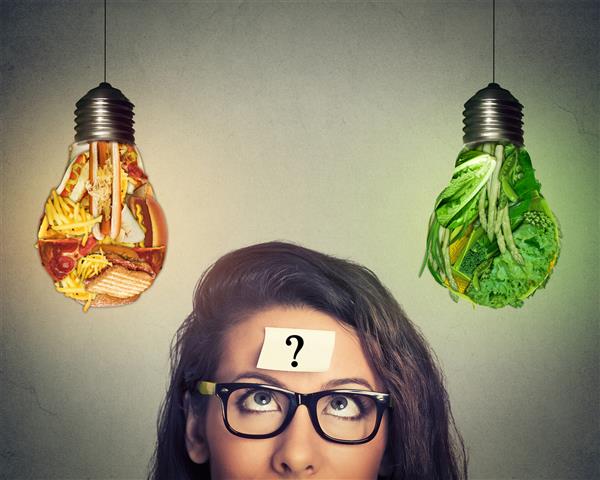 زنی با عینک علامت سوال روی سر دارد و به غذاهای ناخواسته و سبزیجات سبز که به صورت لامپ جدا شده روی پس زمینه خاکستری است نگاه می کند انتخاب رژیم غذایی مفهوم صحیح تغذیه مناسب