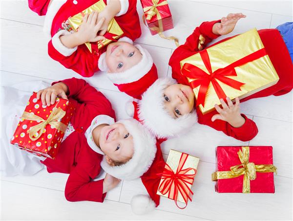 گروهی از سه کودک با کلاه کریسمس با هدیه روی زمین