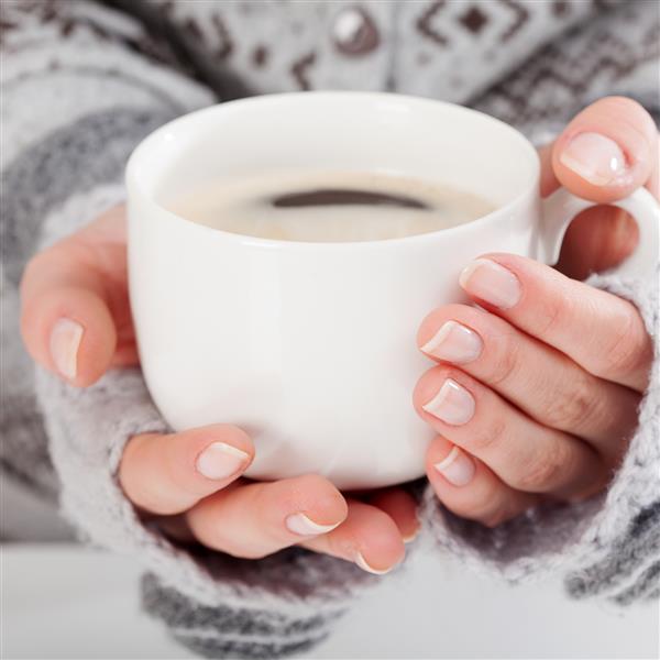 نمای نزدیک از زنی که یک فنجان قهوه داغ در دست دارد