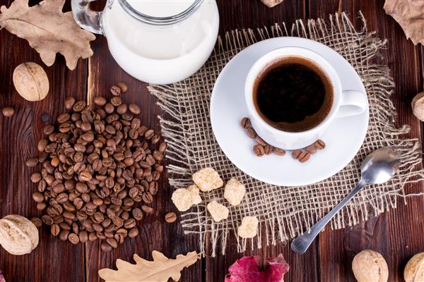 فنجان قهوه خامه دانه های قهوه و شکر عصا روی یک میز