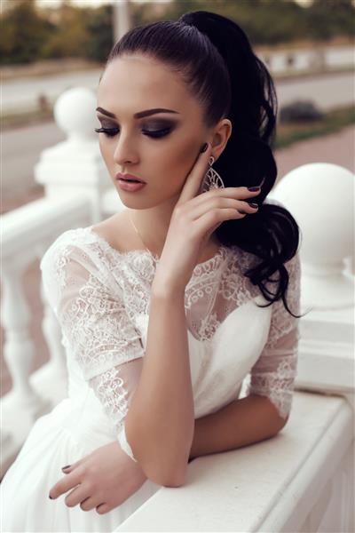 عکس در فضای باز از زن جوان با موهای تیره بلند با لباس عروس توری لوکس