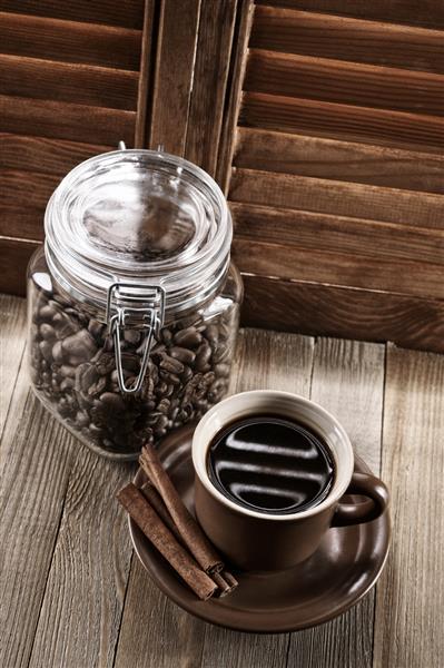 فنجان قهوه با دارچین و لوبیا در ظرف شیشه ای مقابل پنجره با کرکره های چوبی