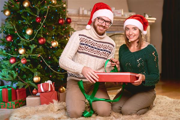 زوج خوشبخت در بسته شدن هدیه عصر کریسمس در کلاه سانتا
