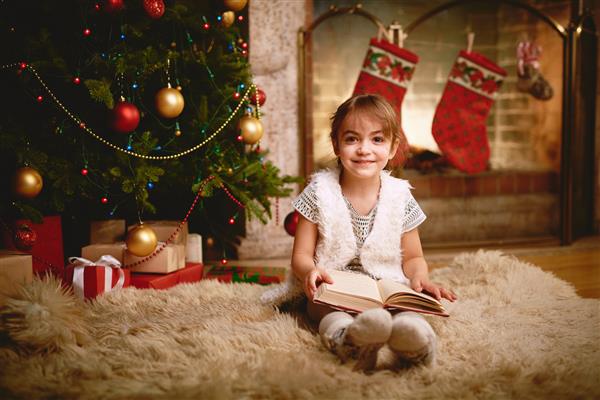 دختر شاد با کتاب که عصر کریسمس به دوربین نگاه می کند