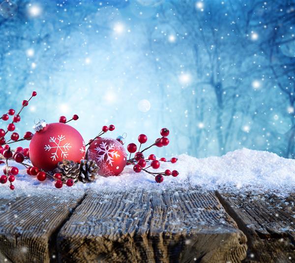 زیور آلات قرمز کریسمس روی میز برفی با بارش برف در پس زمینه
