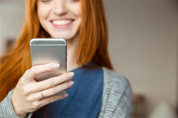 تصویر بریده شده از یک زن مو قرمز خندان با استفاده از تلفن هوشمند