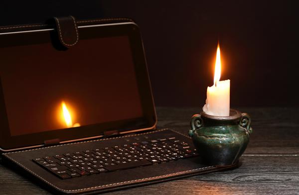 مفهوم خاموشی شمع روشن در نزدیکی لپ تاپ با صفحه خالی و تاریک
