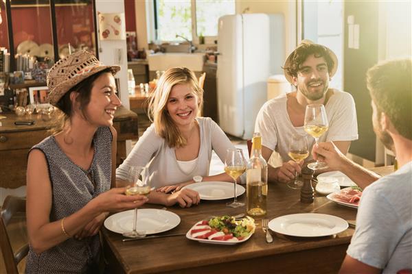 دوستانی که در 30 سالگی خود هستند و یک آپریتیف زیبا روی یک میز چوبی روستایی در یک خانه دوست داشتنی دارند آنها در حال تفریح ​​و صحبت در مقابل لیوان های شراب سفید و موتزارلا گوجه فرنگی - افراد واقعی هستند
