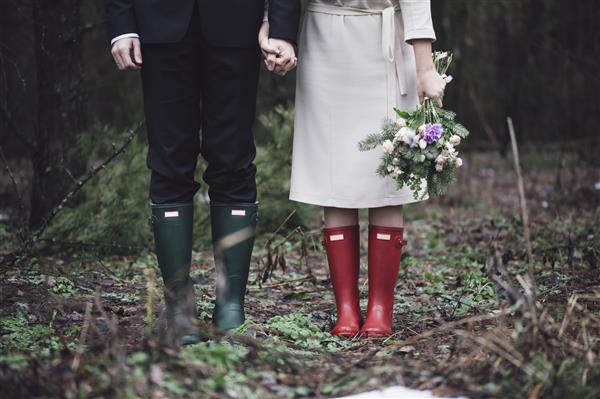زن و شوهر عروسی که با چکمه های لاستیکی رنگارنگ در جنگل ایستاده اند