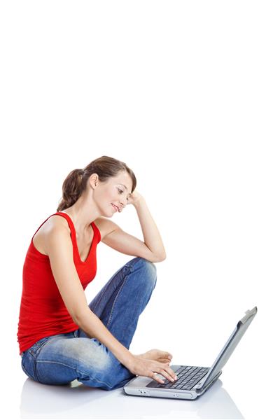 زن جوان زیبا و خوشبختی که روی زمین نشسته و روی لپ تاپ کار می کند
