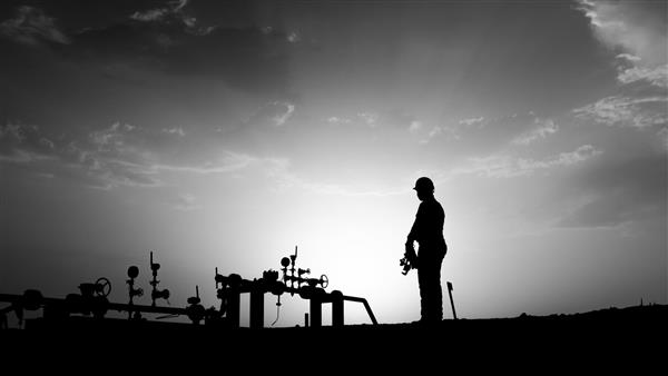 غروب آفتاب و شبح کارگر میدان نفتی که از منیفولد چاه در میدان نفتی نظارت می کند