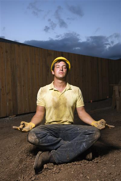 کارگر ساختمانی با لباس زردی به تن دارد در حالت مراقبه یوگا می نشیند