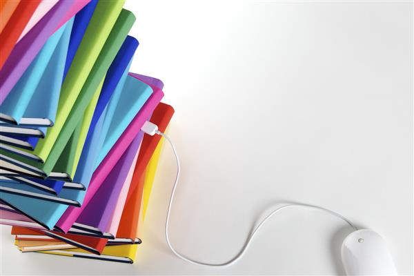 مفهوم یادگیری الکترونیکی - ماوس کامپیوتر به پشته ای از کتابهای رنگارنگ واقعی در پس زمینه سفید نمای بالا متصل می شود