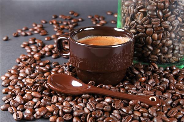 فنجان قهوه قرمز قهوه داغ و دانه های قهوه و دارچین