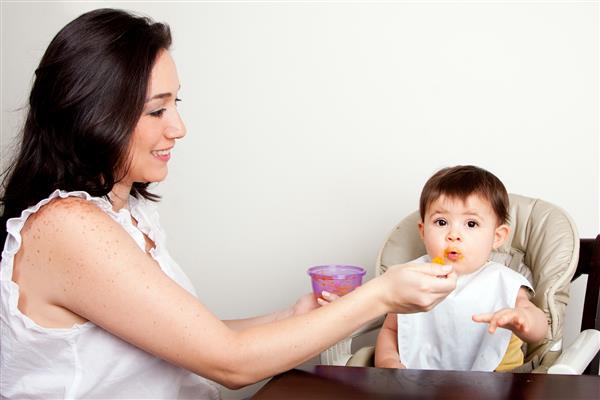 مادر یا پرستار بچه خوشحال و سر بچه خنده رو که غذا میخورد