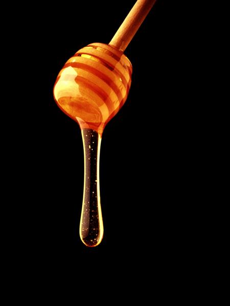 قطره عسل طلایی به آرامی از دلمه عسل چوبی می چکد