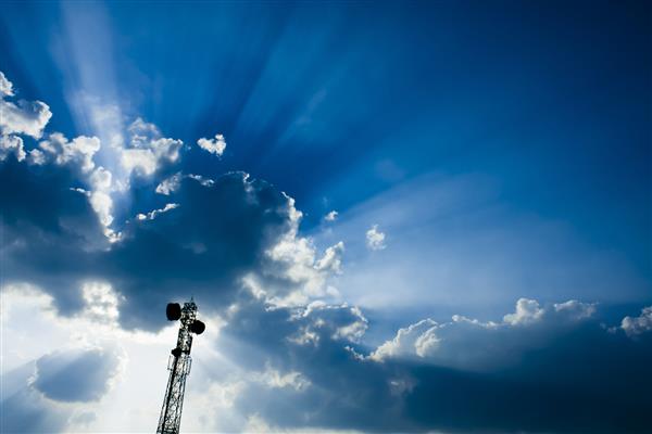 دکل برج مخابراتی با پیوند مایکروویو و آنتن های فرستنده تلویزیون بر فراز آسمان آبی زیبا و پر از ابر و اشعه خورشید