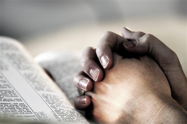 دستان انسان در هنگام دعا بر روی یک کتاب مقدس مقدس بسته شده است - نشان دهنده ایمان و معنویت در زندگی روزمره است