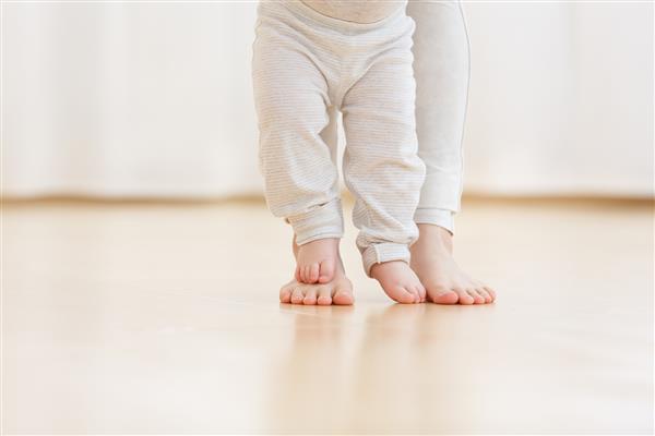 پسر بچه ناز که یاد می گیرد راه برود و اولین قدم هایش را برمی دارد مادر دستش را گرفته است پای کودک از نزدیک بسته می شودفضا را کپی کنید
