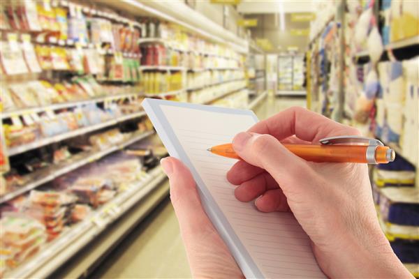 دستی با قلم در حال نوشتن لیست خرید در سوپرمارکت - تمرکز بر روی پیش زمینه