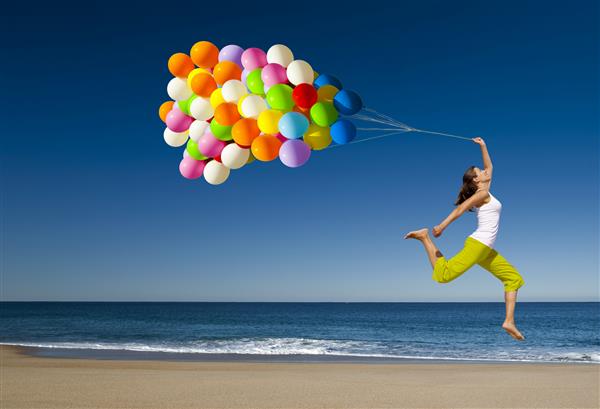 دختری زیبا و ورزشکار با بالن های رنگارنگ که در ساحل می پرند