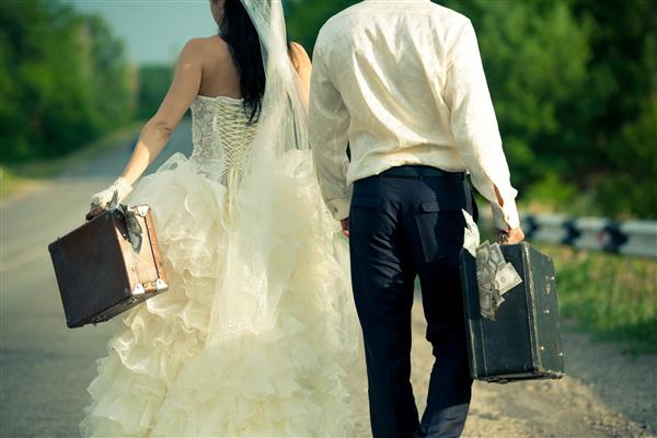 نمای نزدیک زوج جوان تازه عروس با چمدان های پر از پول در جاده
