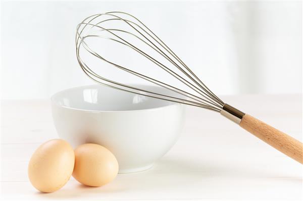همزن تخم مرغ و کاسه روی یک میز سفید