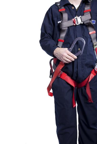 کارگری که لباس های روتختی آبی رنگ و یک مهار محافظ در برابر سقوط و بند برای کار در ارتفاعات پوشیده است