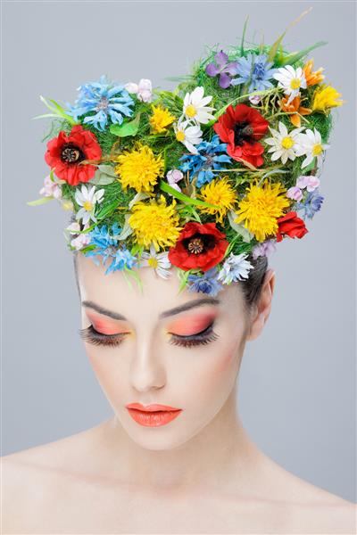 دختر زیبا با گلهای رنگارنگ روی سر و آرایش خلاقانه به پایین نگاه می کند