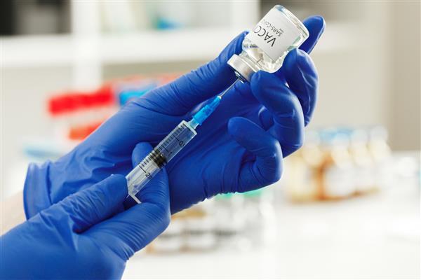 پزشک دستکش های آبی در دست دارد و واکسن کووید -19 را برای واکسیناسیون یک بیمار آماده می کند