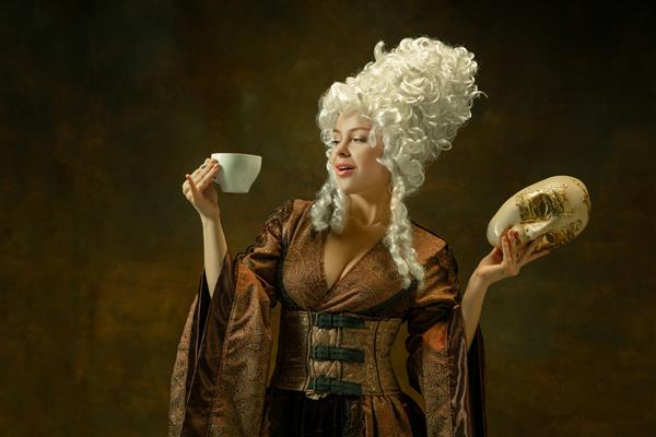 نوشیدن قهوه با ماسک پرتره زن جوان قرون وسطایی با لباس های قهوه ای رنگی روی دیوار تیره مدل زن به عنوان دوشس شخص سلطنتی مفهوم مقایسه دوران مدرن مد