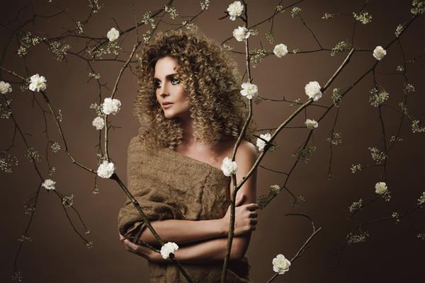 پرتره زن جوان دوست داشتنی با مدل موی آفریقایی و آرایش زیبا با تعداد زیادی گل سفید روی دیوار