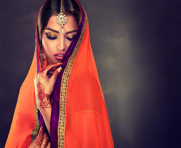 زن جوان هندی مو مشکی با لباس سنتی شیک آرایش عالی با پلک های تذهیب شده خالکوبی حنا روی دستها و جواهرات محلی هند به سبک شرقی