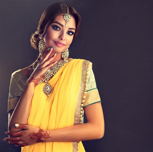 زن جوان موی مشکی پوشیده از مدل ساری زرد شیک با لباس ملی سنتی خال کوبی روی دستان او و مجموعه جواهرات سنتی
