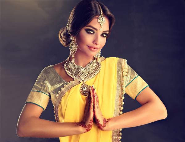دختر زیبای هندی با لباس سنتی ملی پوش خالکوبی روی دستانش نقاشی شده است و مجموعه جواهرات سنتی به سبک کندان در حال نشان دادن یک سلام به ناماست