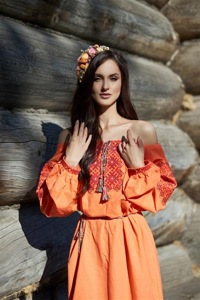 زن اسلاوی زیبا با لباس قومی نارنجی و تاج گل روی سر آرایش طبیعی زیبا