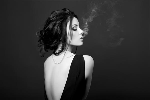 زن سبزه هنری در حال سیگار کشیدن در زمینه تیره با لباس مشکی پرتره کلاسیک از زن قوی با اعتماد به نفس