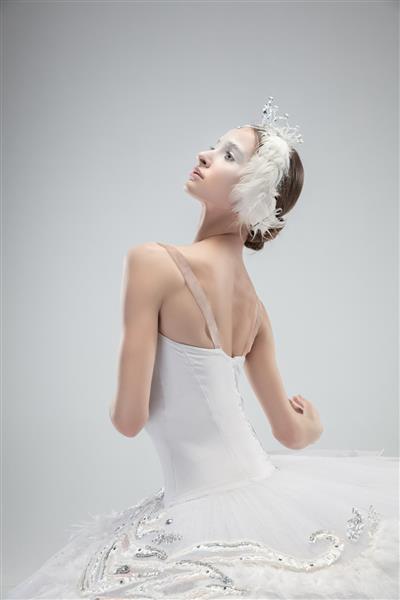 نمای نزدیک رقص بالرین کلاسیک زیبا در زمینه استودیوی سفید زنی با لباسهای نازک مانند قو سفید مفهوم فضل هنرمند حرکت کنش