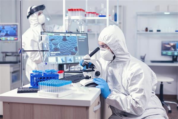 مردی با تجهیزات ppe در حال انجام تحقیقات درباره ویروس کرونا است که در حال بررسی است دانشمندی با لباس محافظ در محل کار با استفاده از فناوری پزشکی مدرن در طول همه گیری جهانی نشسته است