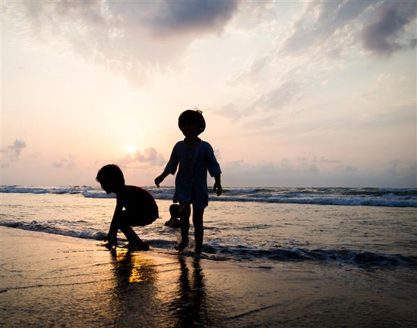 بچه ها که اوقات خوشی را در ساحل دریا نزدیک غروب خورشید سپری می کنند