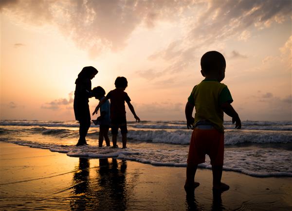 بچه ها که اوقات خوشی را در ساحل دریا نزدیک غروب خورشید سپری می کنند