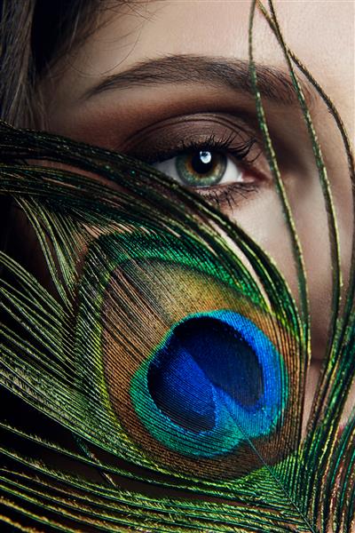 زن عرب شرقی با پر طاووس در دستان نزدیک صورتش زیبایی مد آرایش زنان عرب چشم های زیبا بزرگ پوست صاف زیبا پر طاووس نزدیک چشم
